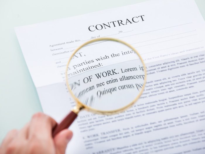 Close-up Of Person's Hand Looking At Contract Through Magnifying Glass