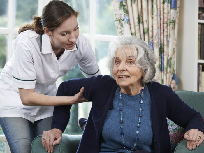 Care Worker Helping Senior Woman To Get Up