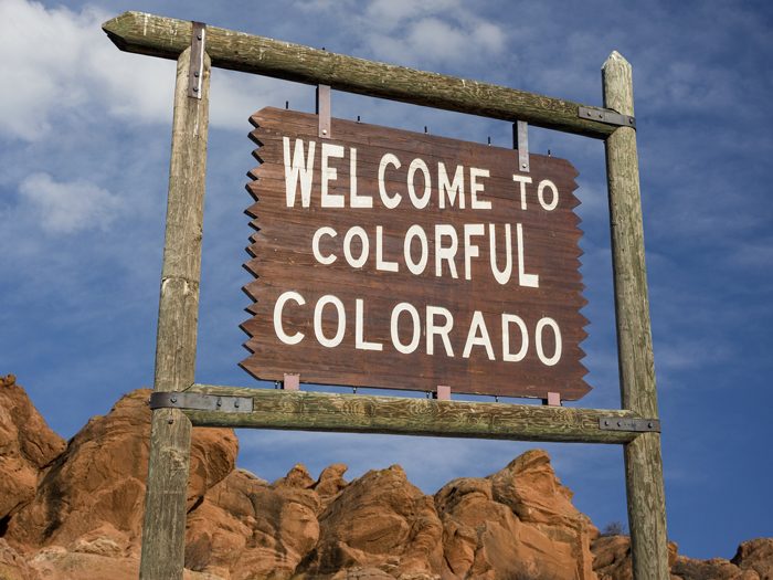welcome to colorful Colorado roadside wooden sign with red sandstone cliff in background